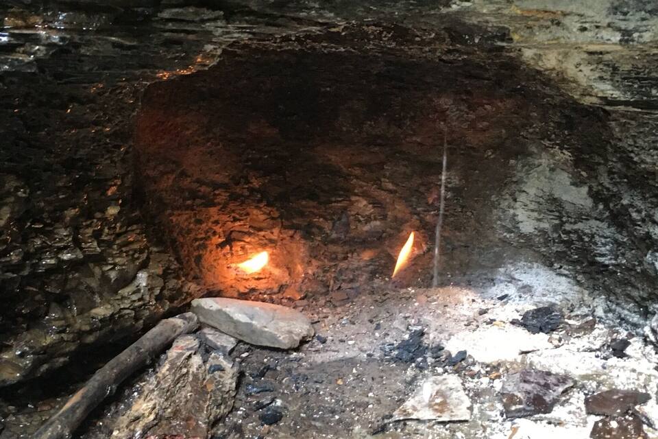 A cave interior with a fire burning in the center, surrounded by rocky walls and debris.
