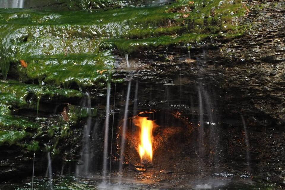 A waterfall cascading over moss-covered rocks with a visible fire at the base.