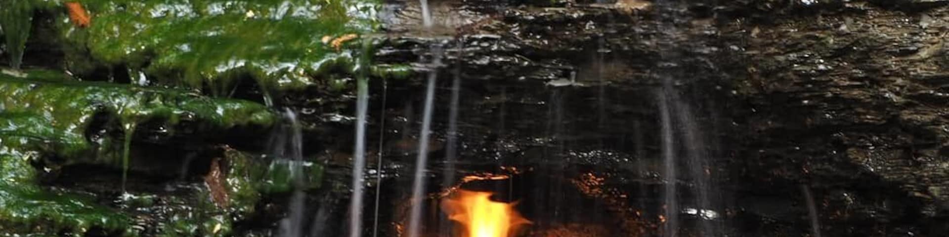 This is Eternal Flame Falls (aka Chestnut Ridge Falls). This waterfall has an unexpected twist, there is a natural gas vent behind the falls that maintains a flame.
A surreal experience to hear the flame flickering over the sound of the cascading water.