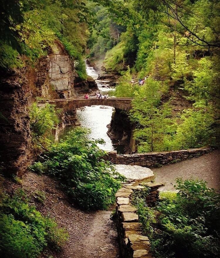 Un puente de piedra sobre un río, rodeado de vegetación exuberante y acantilados rocosos.