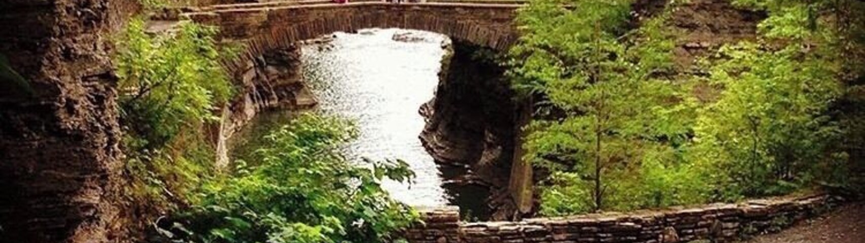 Un puente de piedra sobre un río, rodeado de vegetación exuberante y acantilados rocosos.