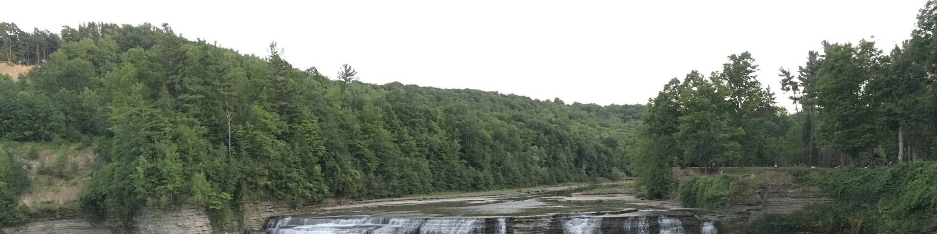 A multi-tiered waterfall cascading down a rocky cliff surrounded by dense forest.