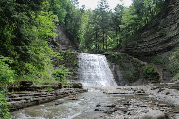 A waterfall cascading into a river surrounded by dense forest and rocky cliffs.