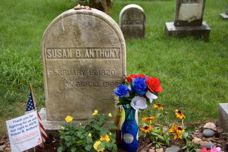 A gravestone with the name Susan B. Anthony, surrounded by flowers and a votive candle.
