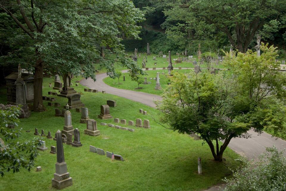 A cemetery with numerous gravestones, a winding path, and lush greenery.
