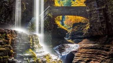 A waterfall cascading through a rocky gorge with a stone bridge arching over the water.