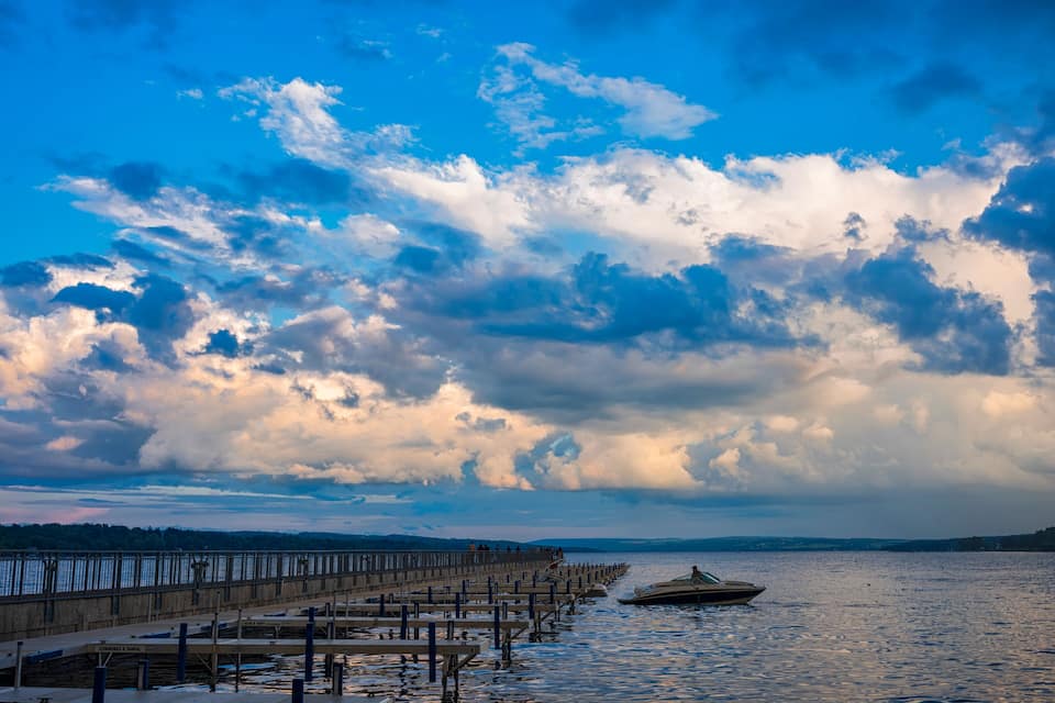 A pier extending into a body of water with a boat docked at the end, under a partly cloudy sky.