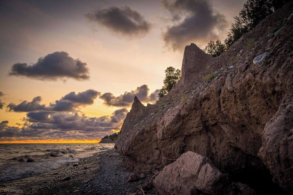 A rocky coastline with a sunset and clouds.