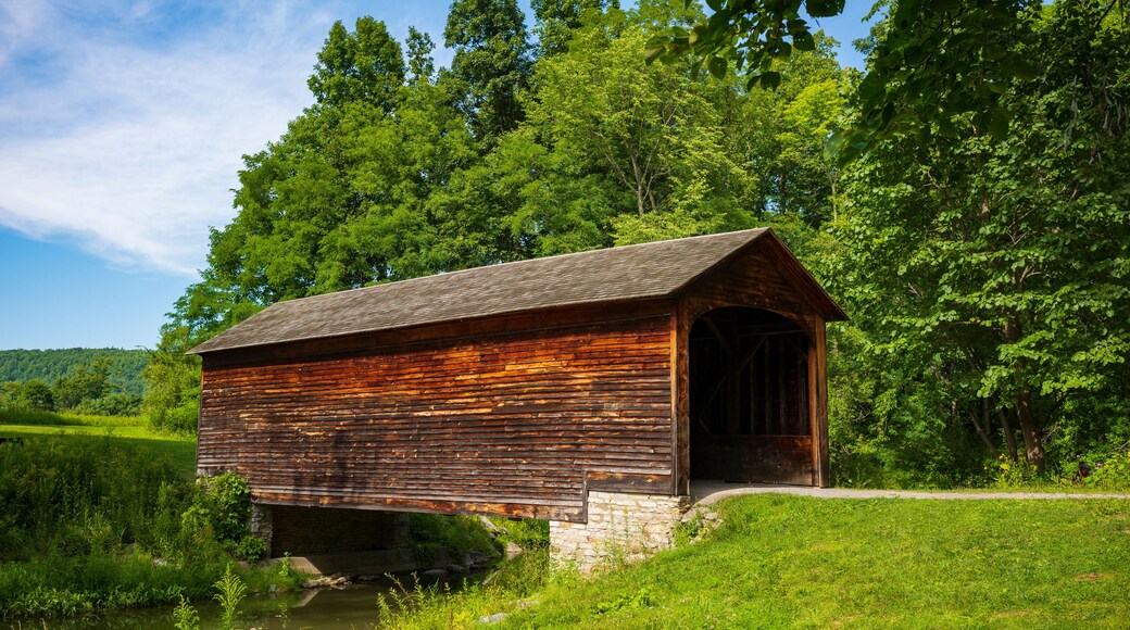 The Hyde Hall Covered Bridge, built in. 1825 and is the oldest existing covered bridge in the U.S., rests at the end of a dirt road during a summer day.