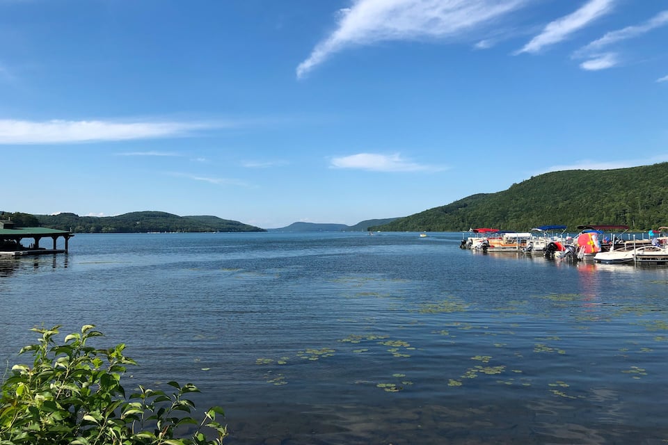 A calm lake with boats, a dock, and a green hill in the background.