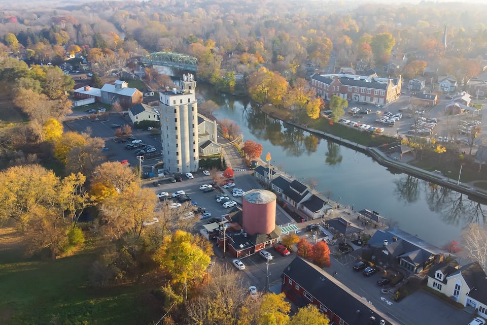 An aerial view of a town with a river, a bridge, and autumn-colored trees.