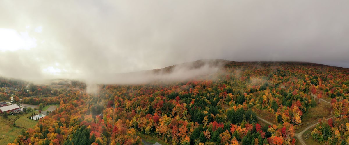Paisagem montanhosa com folhagem outonal, um celeiro vermelho e uma estrada sinuosa.