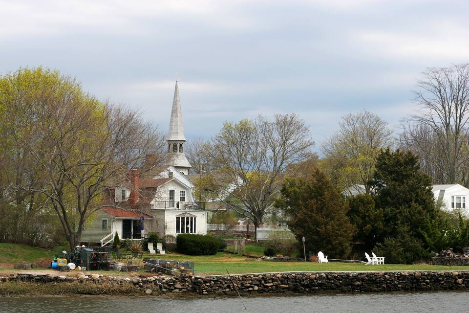 A white church with a steeple, surrounded by trees and a stone wall.