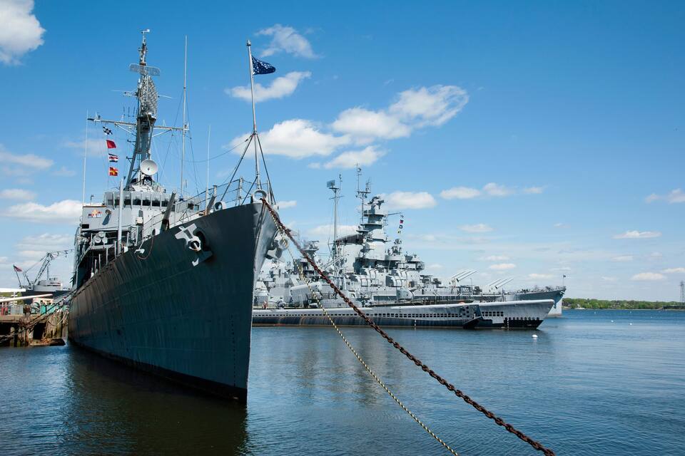 Un gran buque de guerra atracado en un puerto, con cielo despejado y aguas tranquilas.