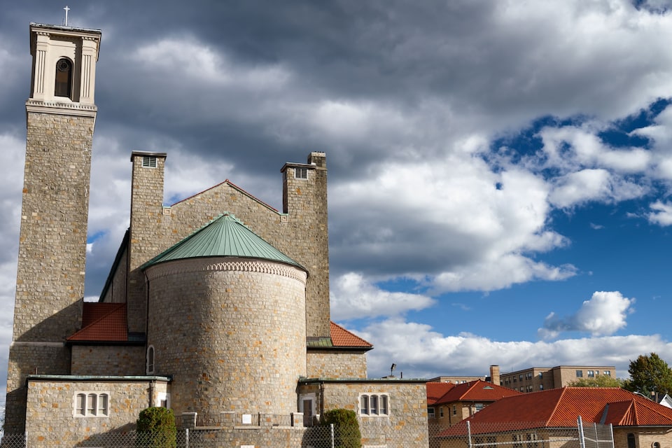 A historic stone church with a bell tower and a green-tiled roof.
