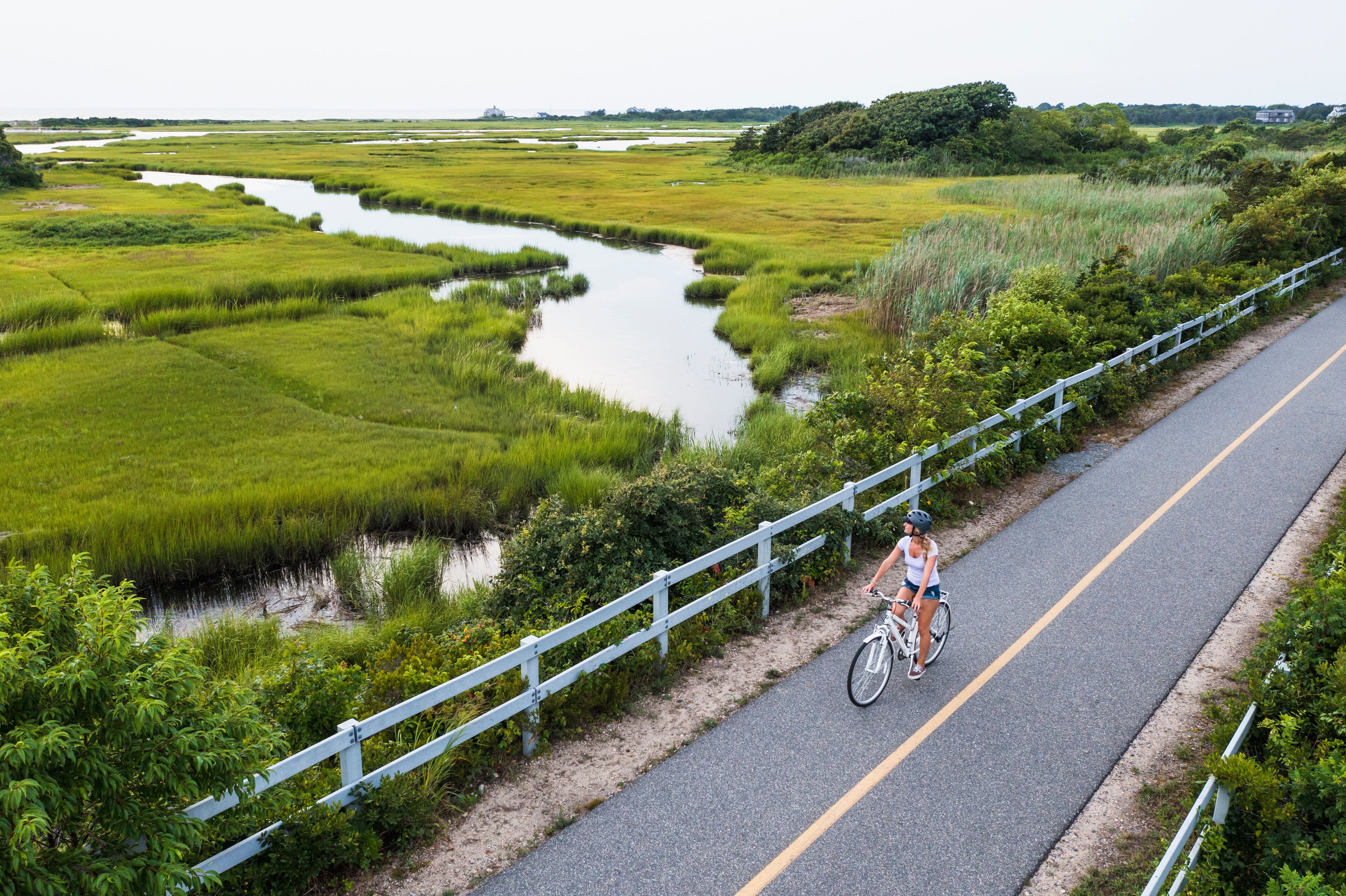 Aerial drone of Woman biking through Cape Cod Marshes bike path