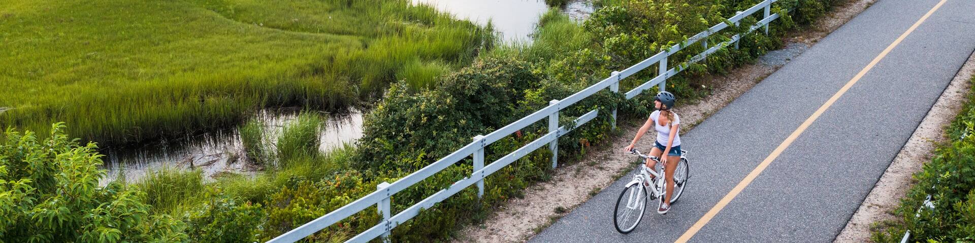 Aerial drone of Woman biking through Cape Cod Marshes bike path