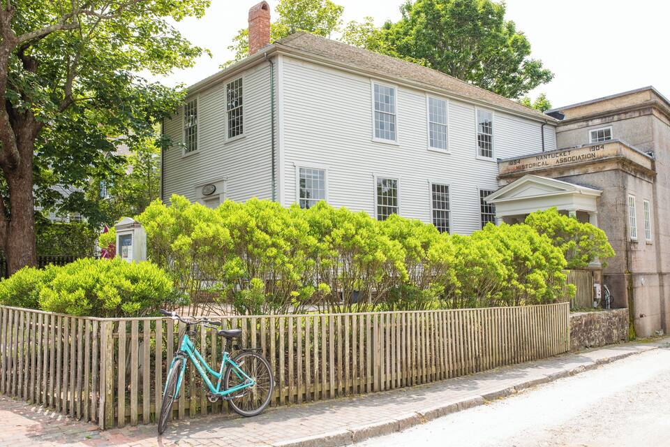 Una casa blanca històrica amb una tanca de fusta i una bicicleta aparcada al davant.