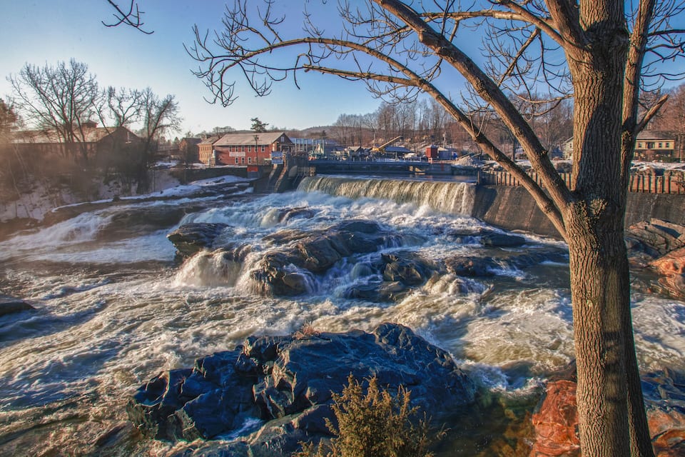 A waterfall with rushing water, surrounded by trees and buildings.