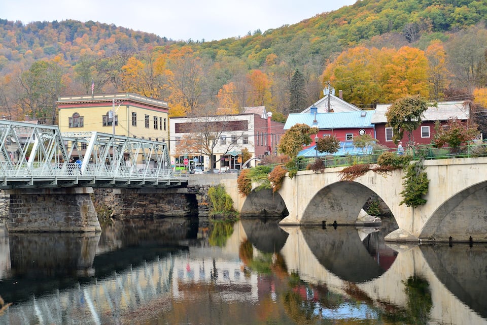 A bridge over a river with autumn-colored trees in the background.