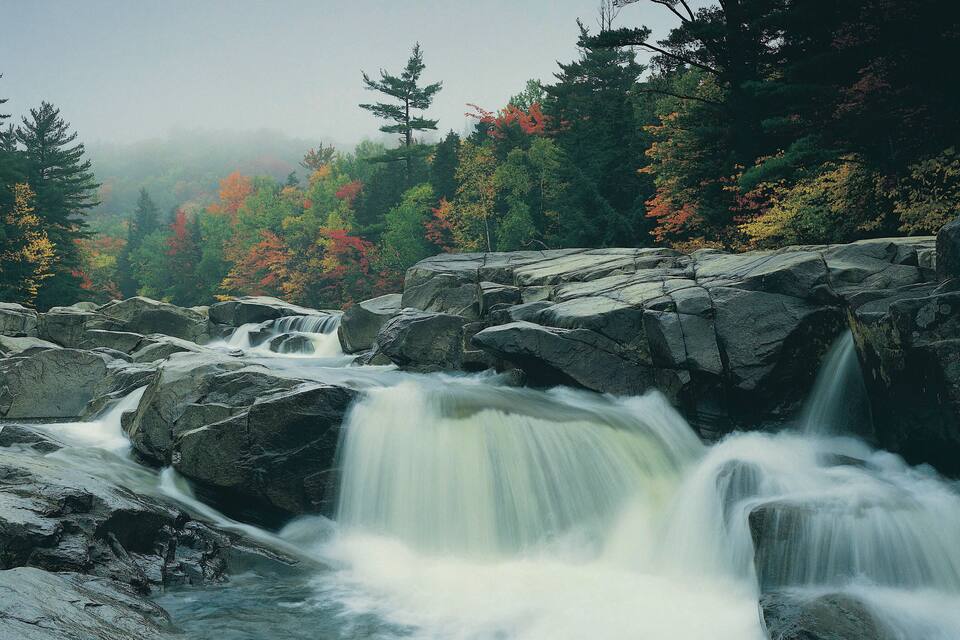 A waterfall cascading over rocks in a forested area with autumn foliage.