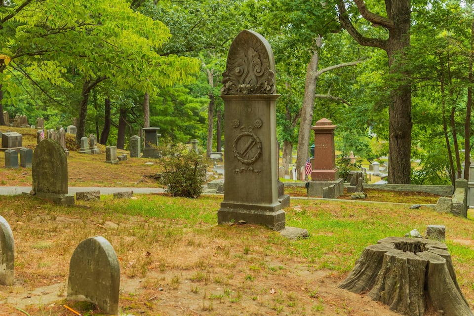 Um cemitério com várias lápides, incluindo uma proeminente com um relógio e uma bandeira.