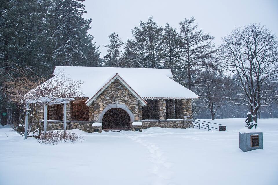 A stone chapel with a snow-covered roof and a statue in front.