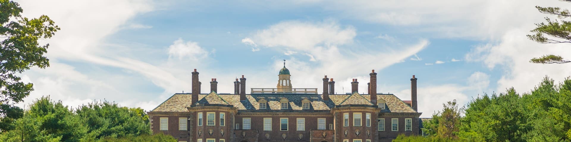A large stately building with a green lawn, a central dome, and a symmetrical facade.