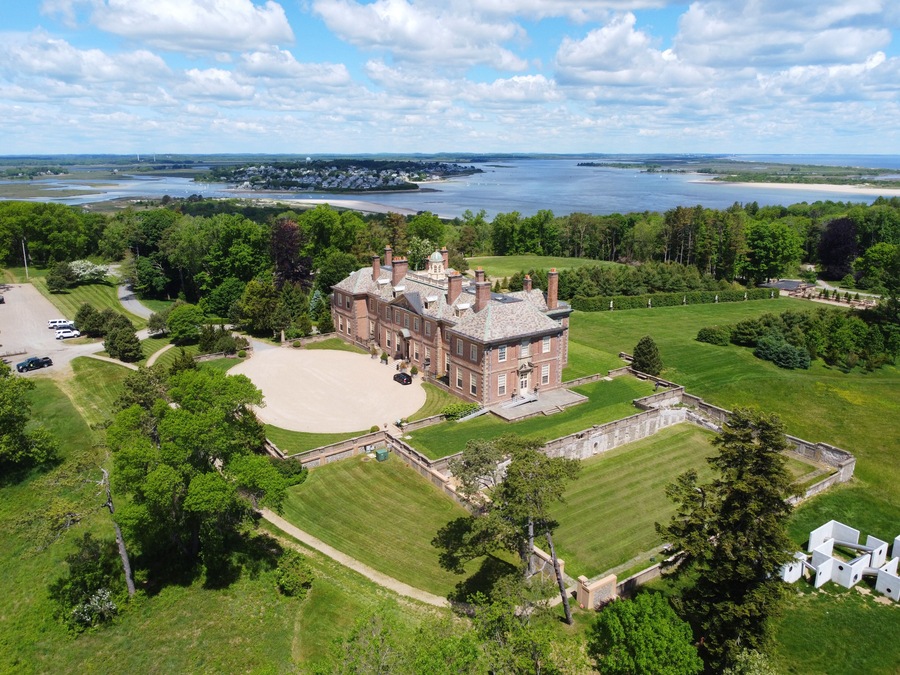 A large estate with a prominent brick building, expansive lawns, and a body of water in the background.