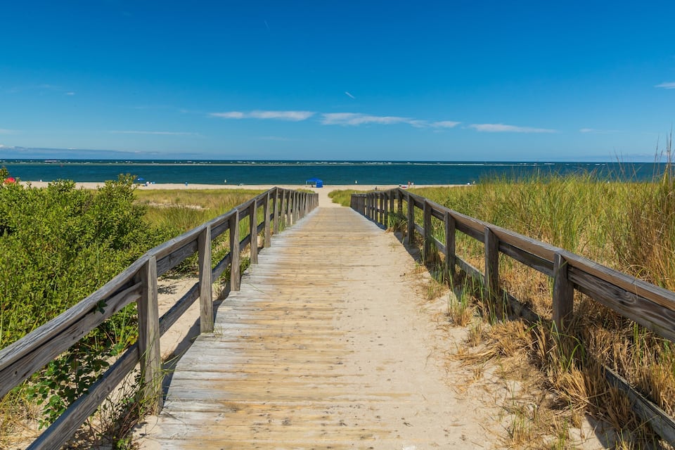 A wooden boardwalk leading to a beach with a clear blue sky.