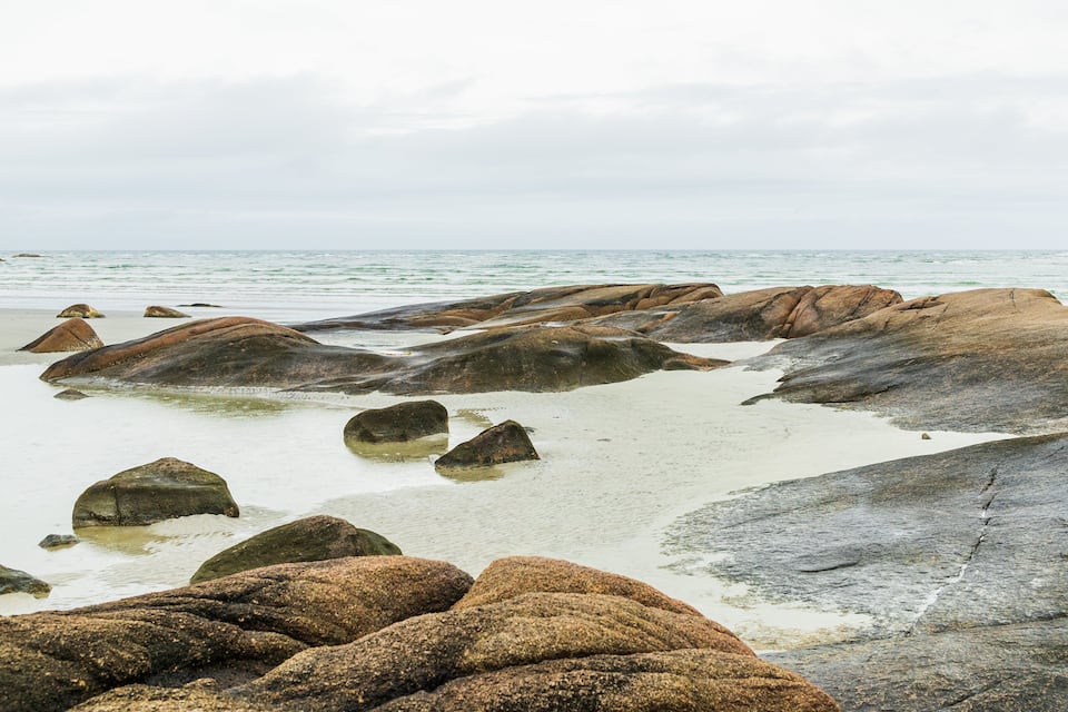 Een rotsachtige kustlijn met grote rotsblokken en rustig water.