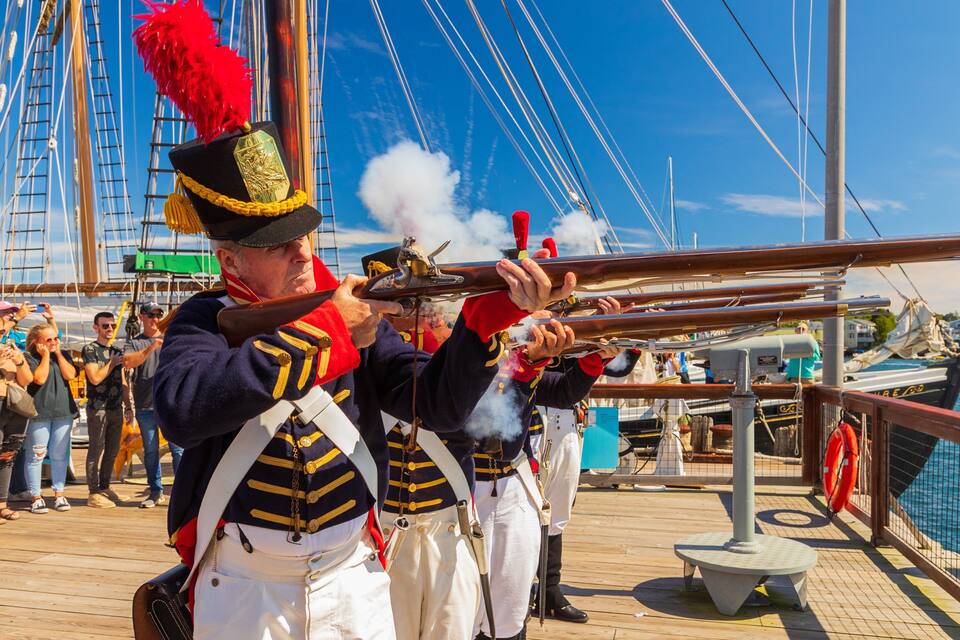 A person in a naval uniform firing a cannon on a ship.