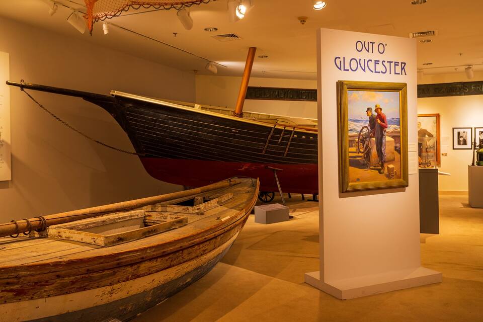 A museum exhibit with a large wooden boat and a painting titled 'Out o' Gloucester'.