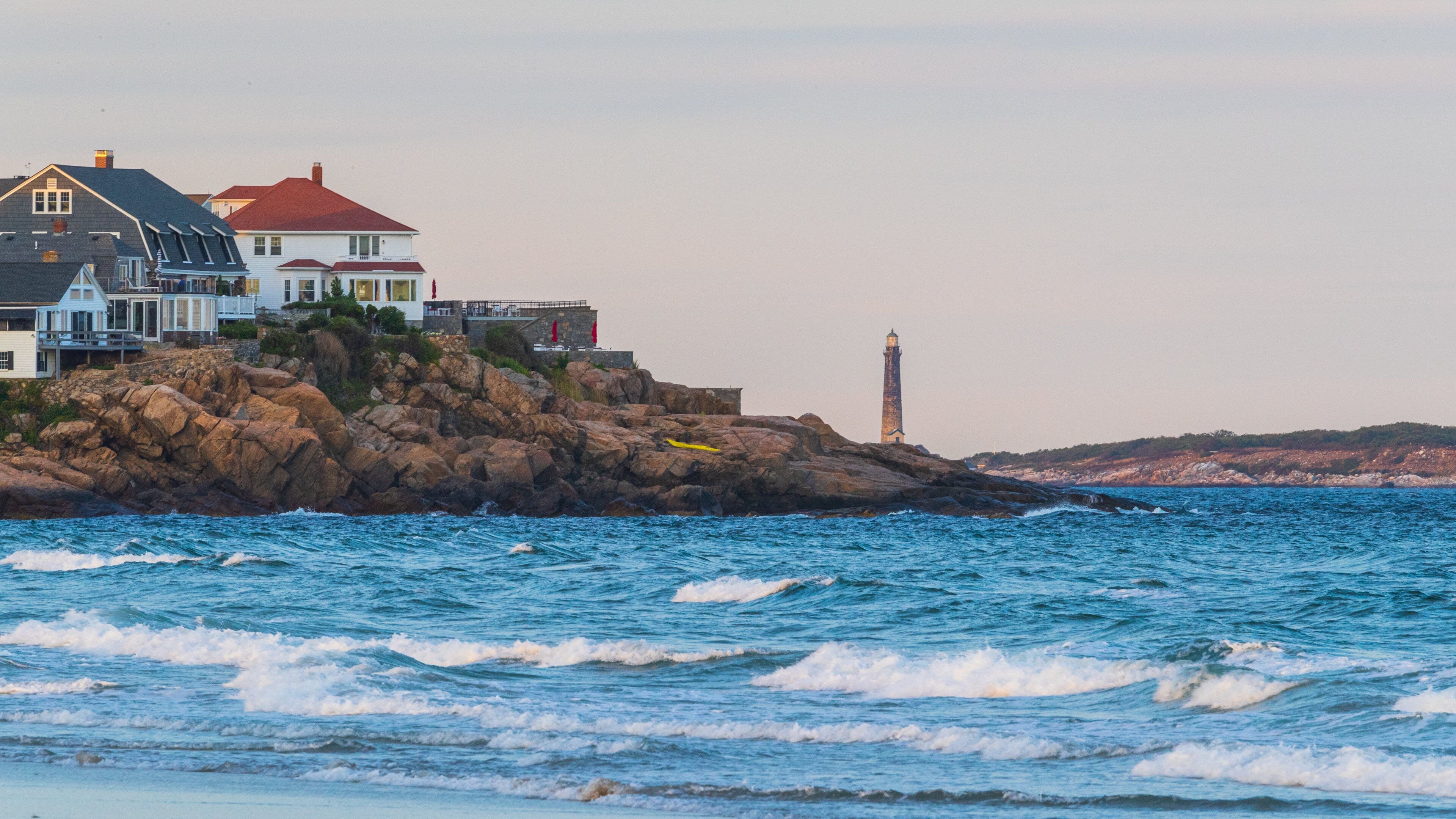A coastal scene with a lighthouse, rocky shoreline, and houses on the cliff.