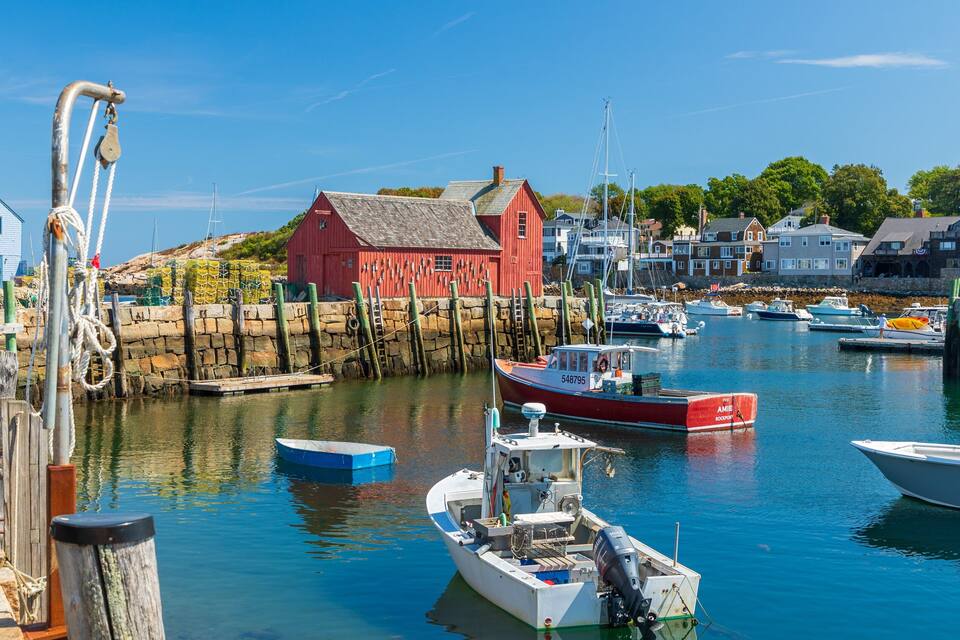 Un port amb barques, un edifici vermell i cases al llarg de la riba.