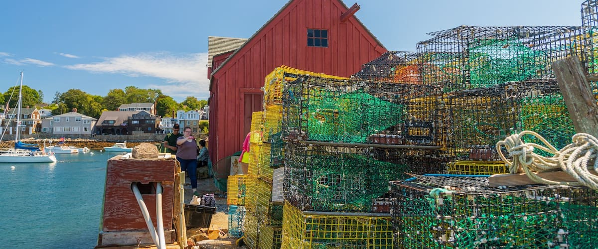Un bâtiment rouge situé près d’un port, avec des casiers à homards empilés.