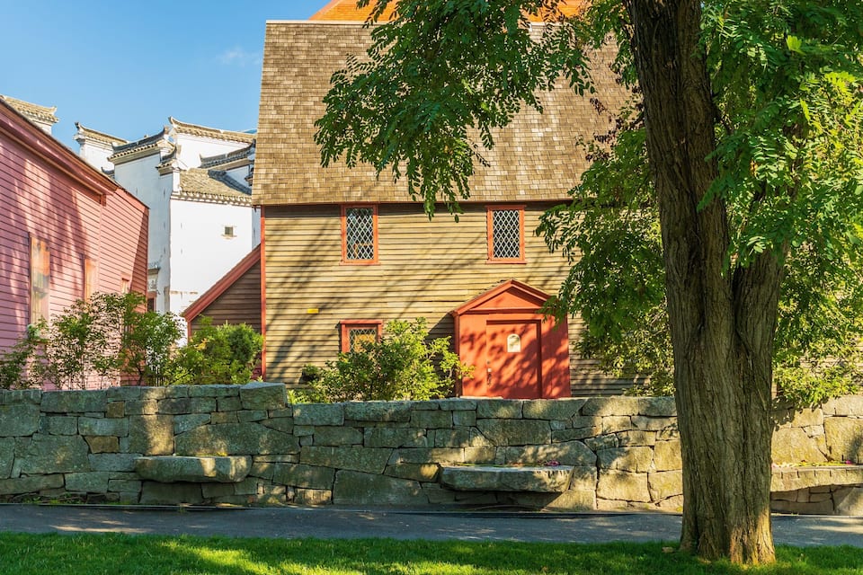 A historic building with traditional architecture, a stone wall, and a tree in the foreground.
