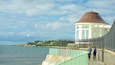 A coastal walkway with a white tower and a metal fence.
