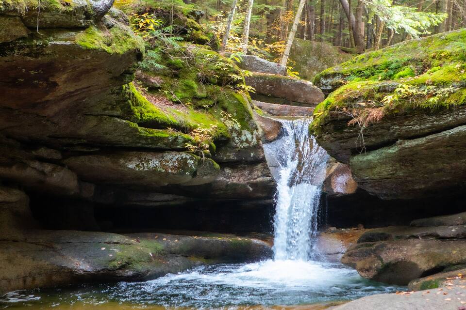 A waterfall cascading over moss-covered rocks in a forested area.