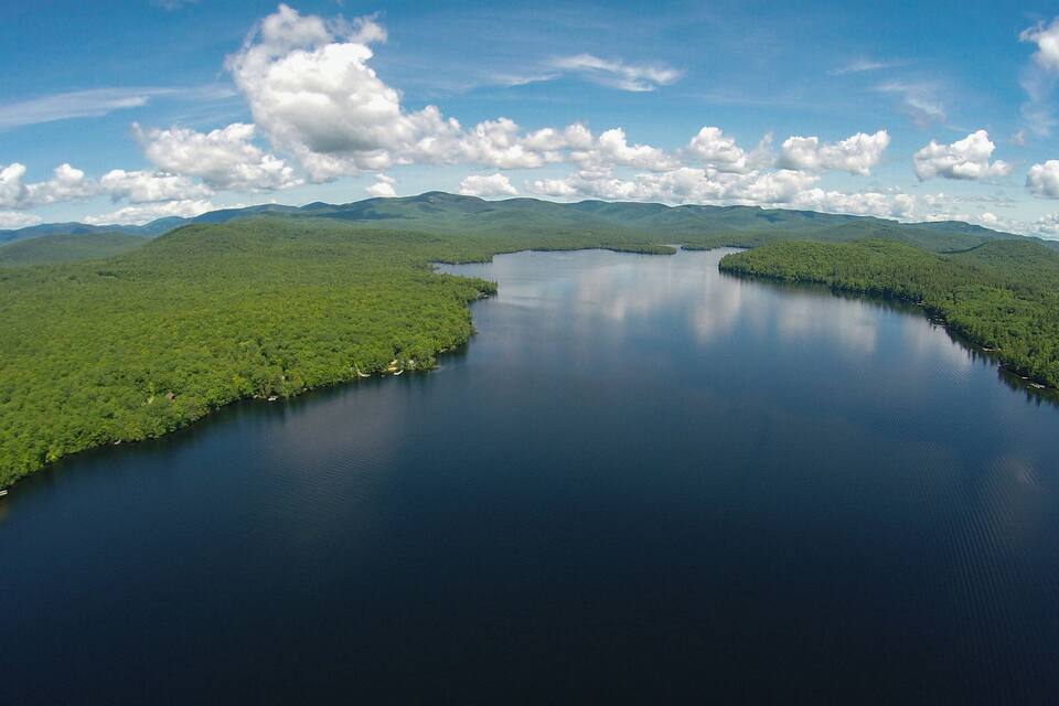 A large lake surrounded by dense green forest and mountains under a partly cloudy sky.
