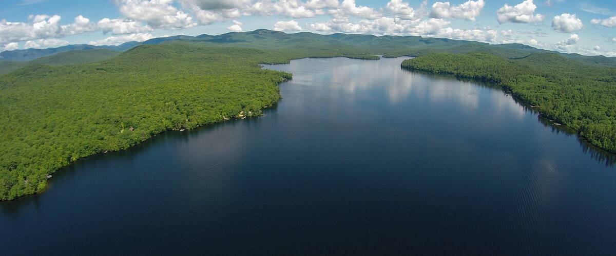 A large lake surrounded by dense green forest and mountains under a partly cloudy sky.