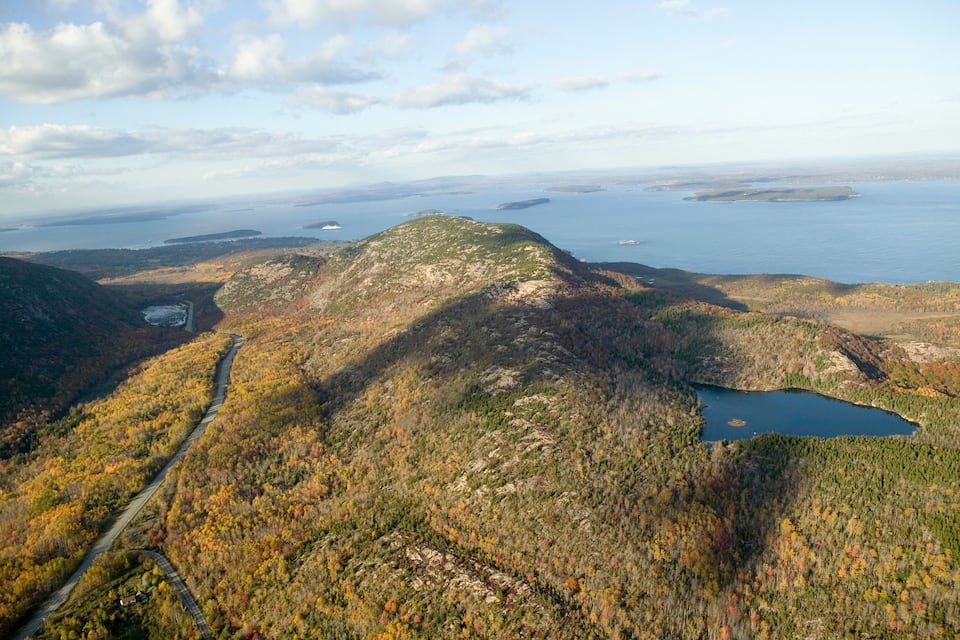Eine gebirgige Landschaft mit einer gewundenen Straße, einem See und fernen Inseln.
