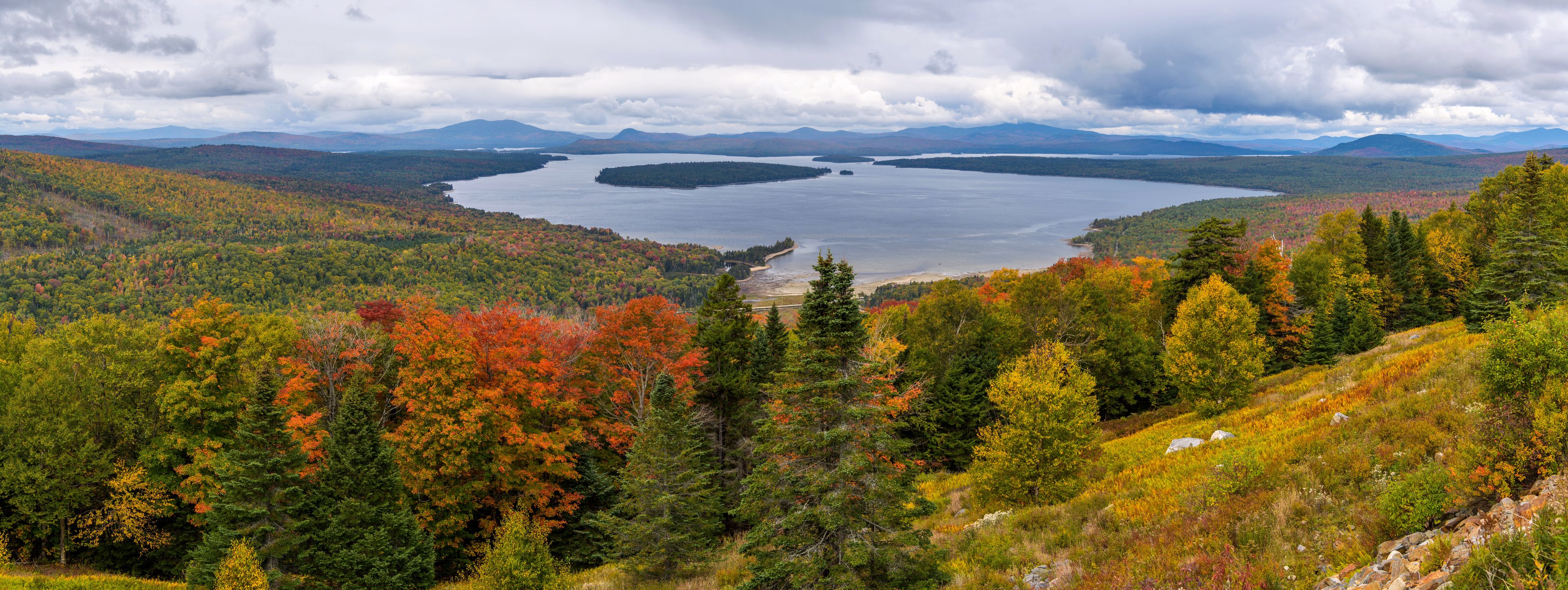 Height of Land - A panoramic overview of Mooselookmeguntic Lake and its surrounding rolling hills on a colorful but stormy Autumn day, as seen from Height of Land at side of Route 17, Maine, USA.