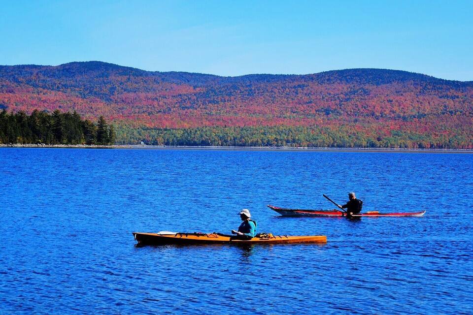 Two canoes on a calm lake with a forested mountain in the background.
