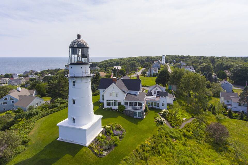 Un faro blanco rodeado de abundante vegetación y casas.