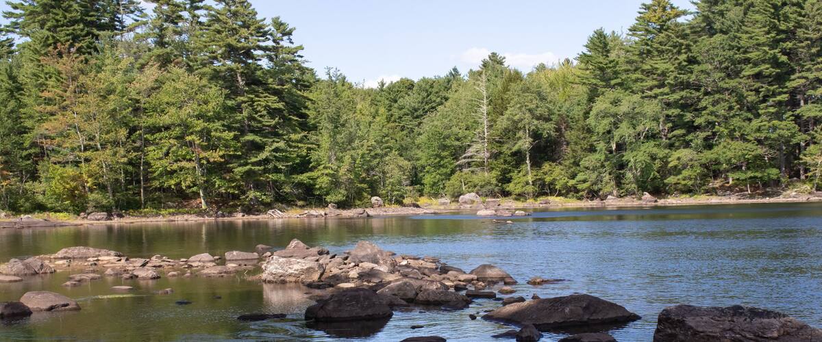 beautiful view of Megunticook Lake in Maine. Large rocks surrounded by clear blue water with forest in background