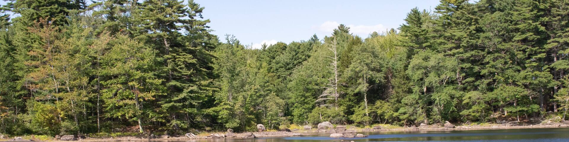 beautiful view of Megunticook Lake in Maine. Large rocks surrounded by clear blue water with forest in background