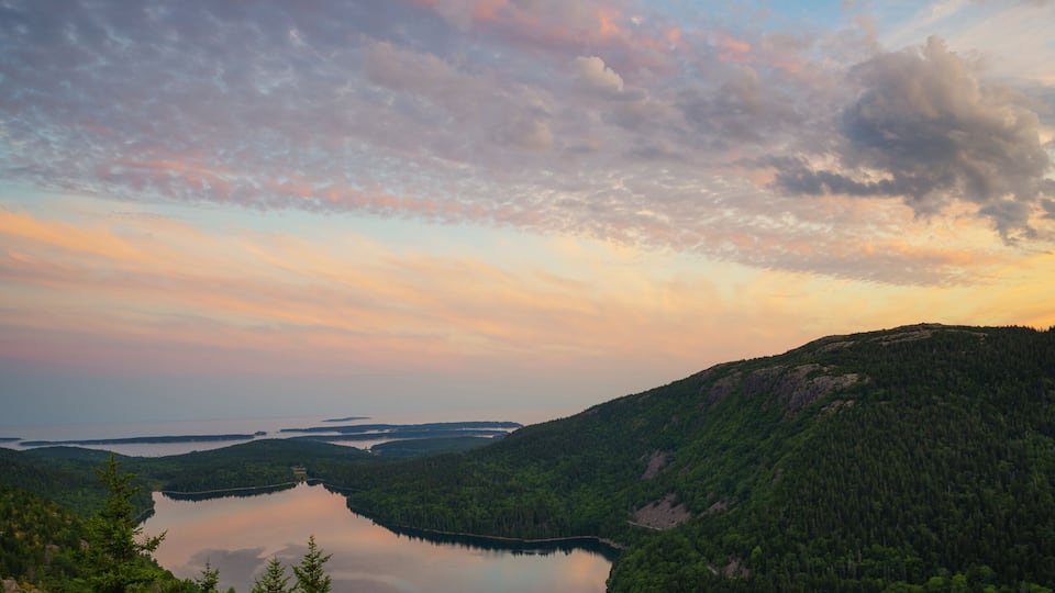 A lake surrounded by forested hills and a clear sky.