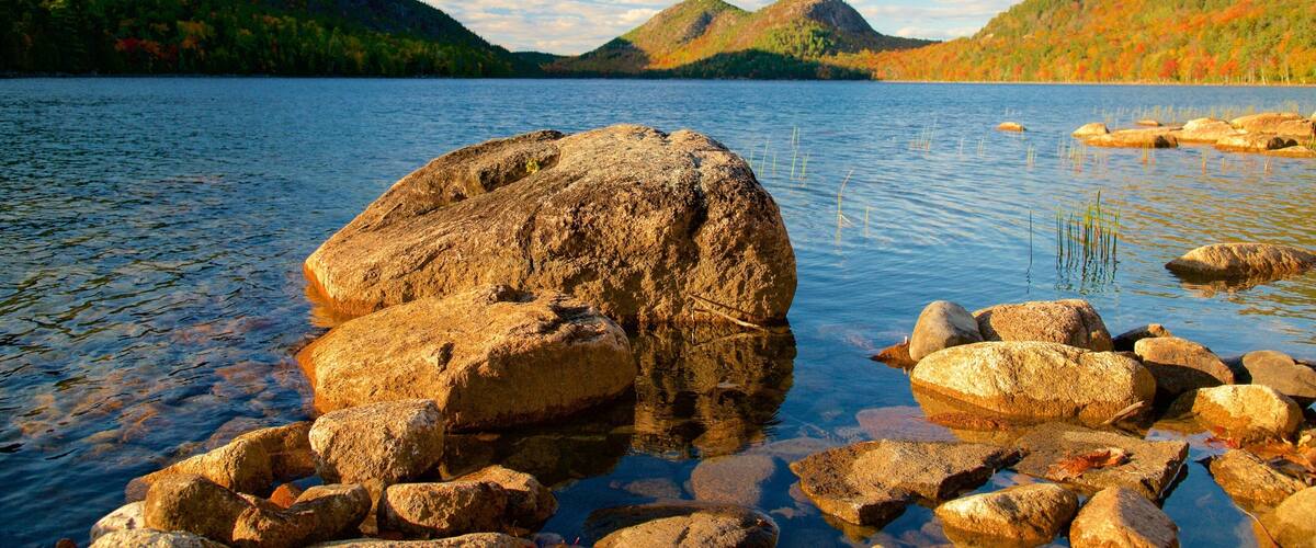 A lake with large rocks in the foreground and mountains in the background.