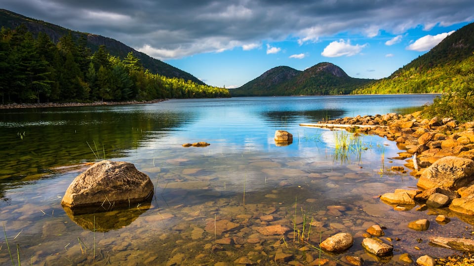 A calm lake surrounded by mountains and clear water with visible rocks and vegetation.